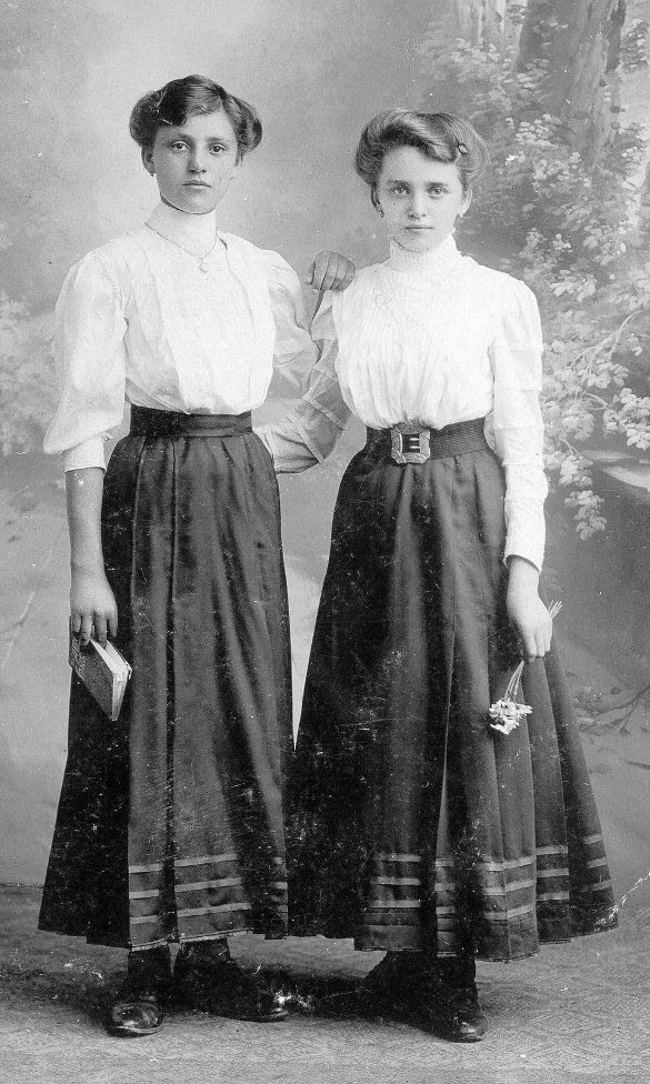 two women standing next to each other in long skirts