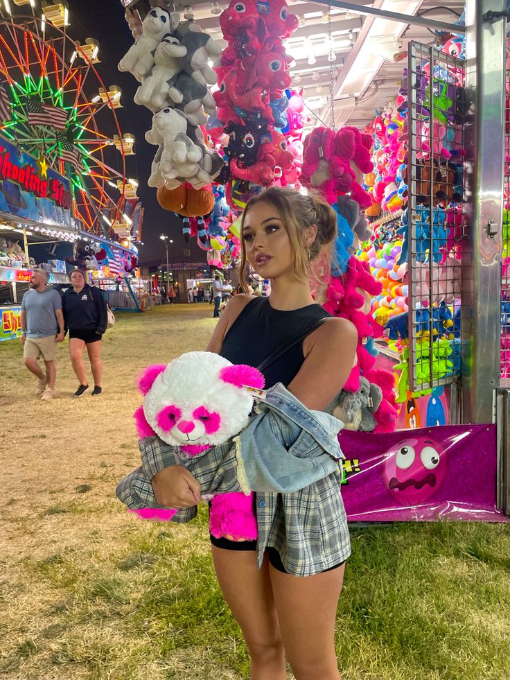 a woman holding a teddy bear in front of a carnival ride