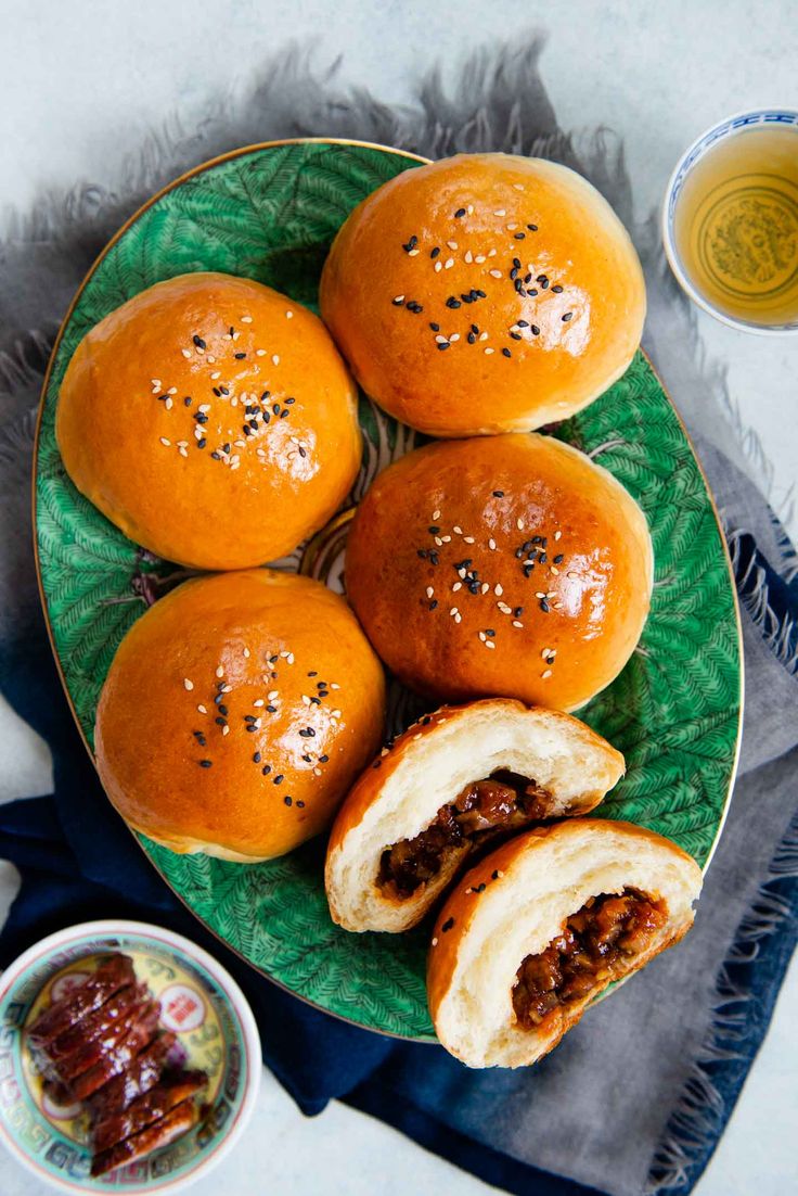 several buns with meat in them on a green plate next to some dipping sauce