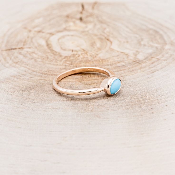 a gold ring with a turquoise stone in the middle on top of a wooden surface