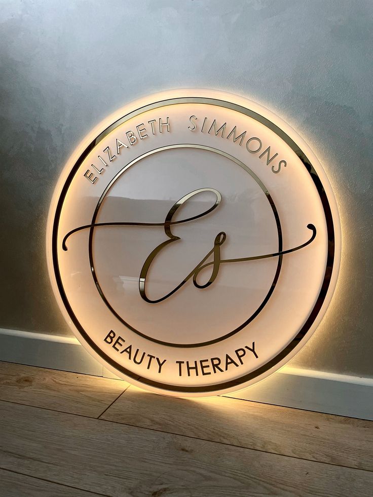 the logo for elizabeth simon's beauty therapy is illuminated in white and gold on a wall