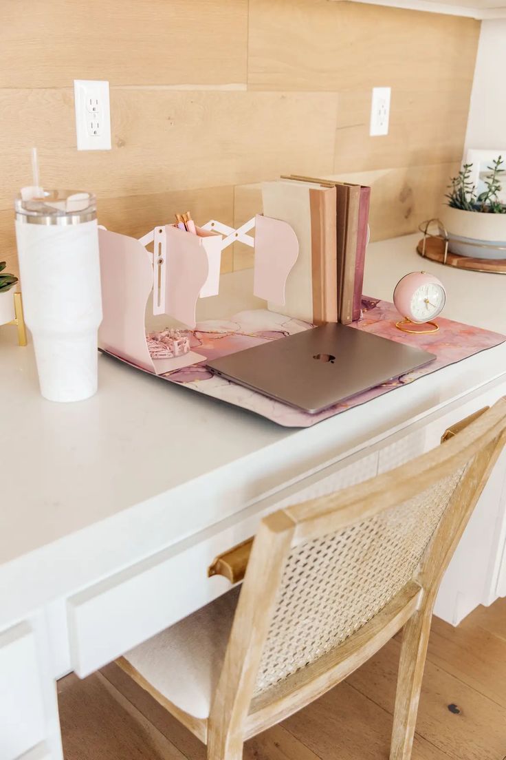 a white desk topped with a laptop computer sitting on top of a wooden table next to a cup