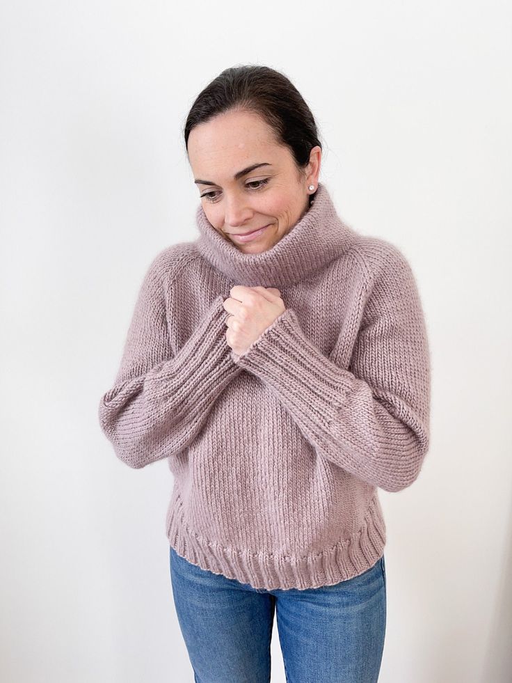 a woman wearing a pink sweater and blue jeans standing in front of a white wall