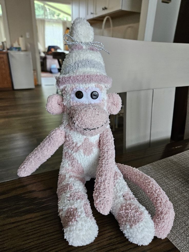 a pink and white stuffed monkey with a hat on it's head sitting on a table