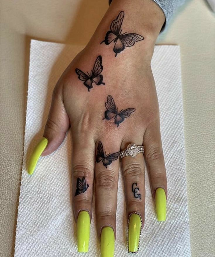 a woman's hand with yellow nail polish and butterflies on the ring finger tattoo