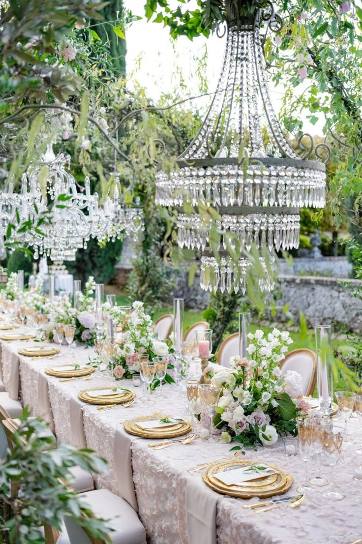 an outdoor table set up with chandelier and flowers on the table for a formal dinner