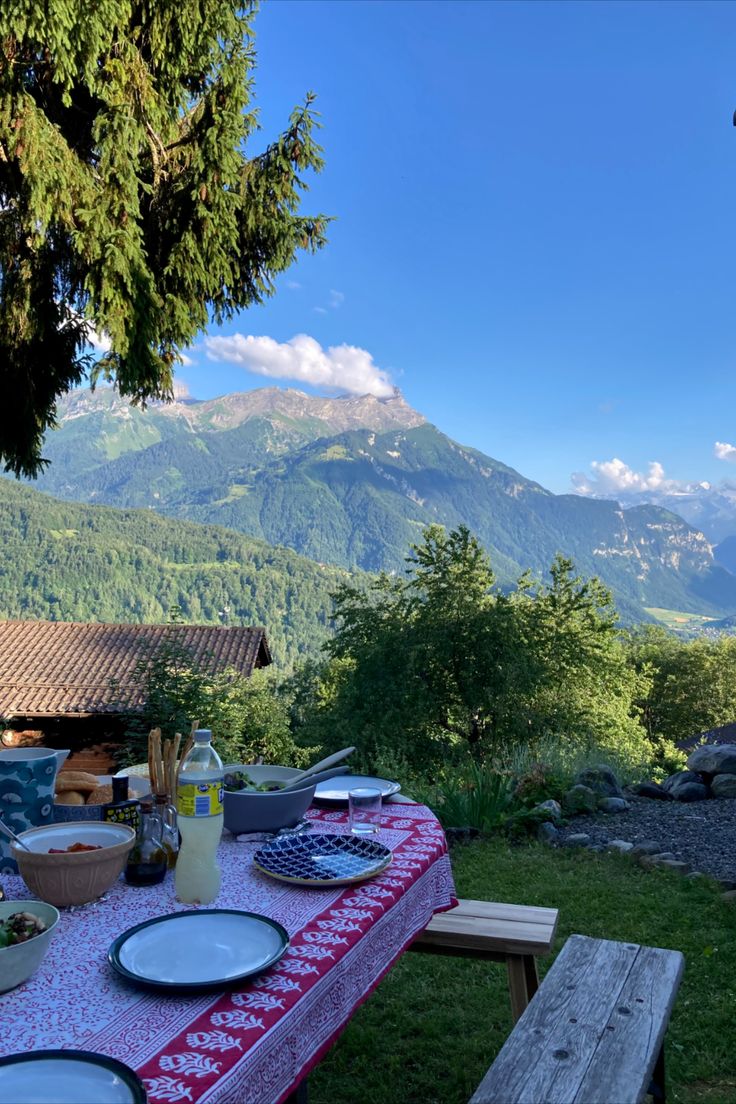 a picnic table with plates and utensils on it in front of a mountain view