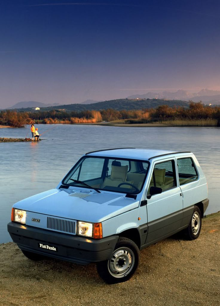 a blue car parked next to the water with a man in a boat behind it