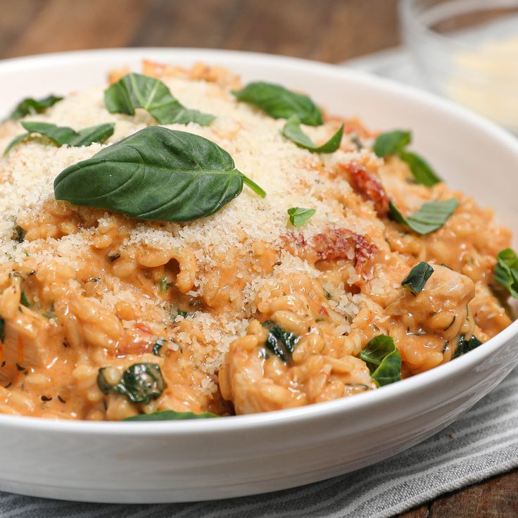 a pasta dish with spinach and cheese in a white bowl on a wooden table