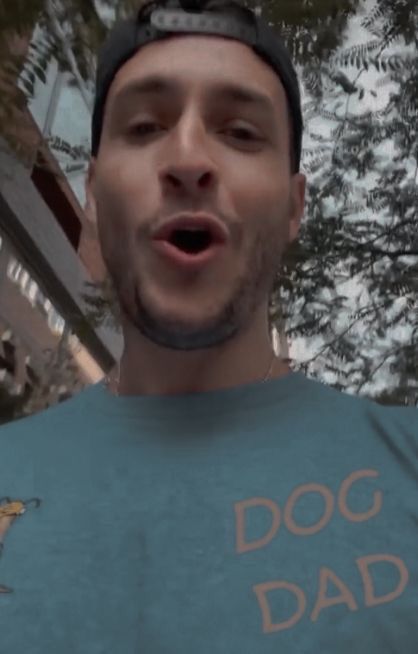 a man making a funny face while wearing a dog dad t - shirt in front of some trees