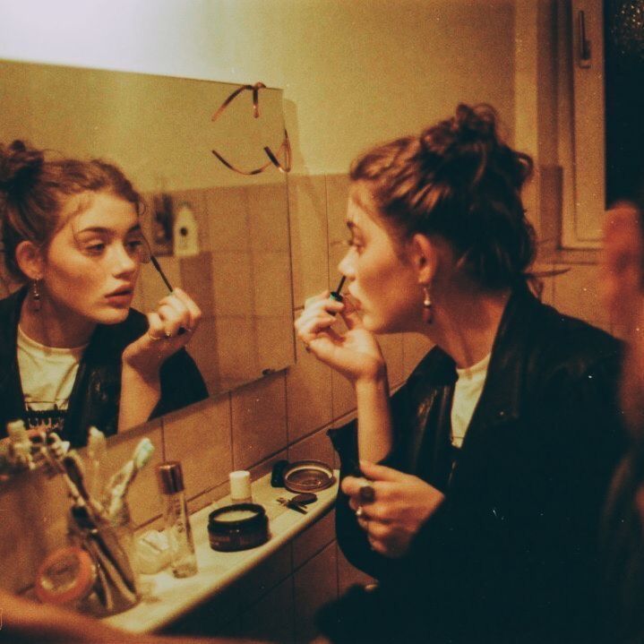 two women sitting in front of a bathroom mirror brushing their teeth and looking into the mirror