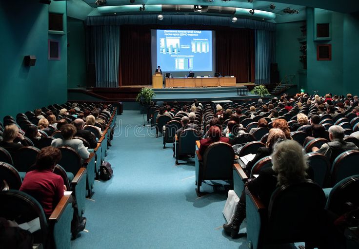 an auditorium full of people sitting in chairs and watching a presentation on a large screen