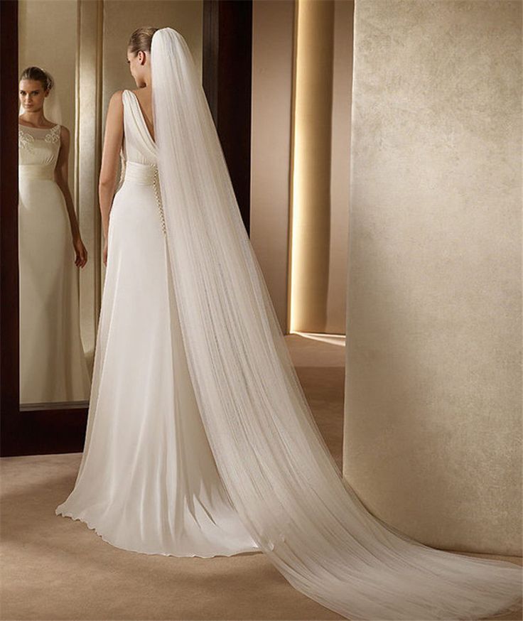 a woman in a wedding dress standing next to a mirror with her veil pulled back