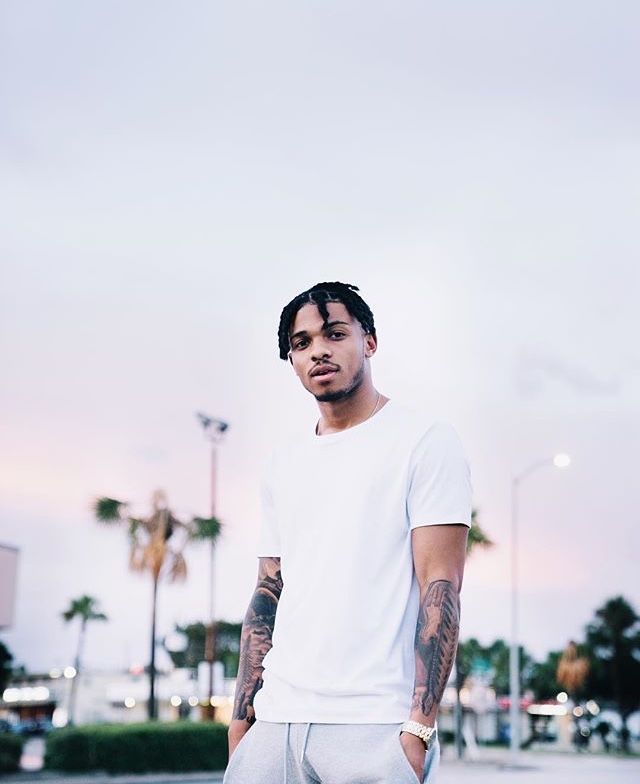 a man with tattoos standing on the street in front of some palm trees and buildings