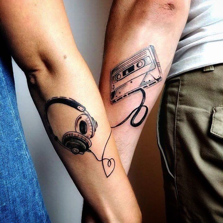 two people with tattoos on their arms holding each other's hands and one has a cassette tape attached to it