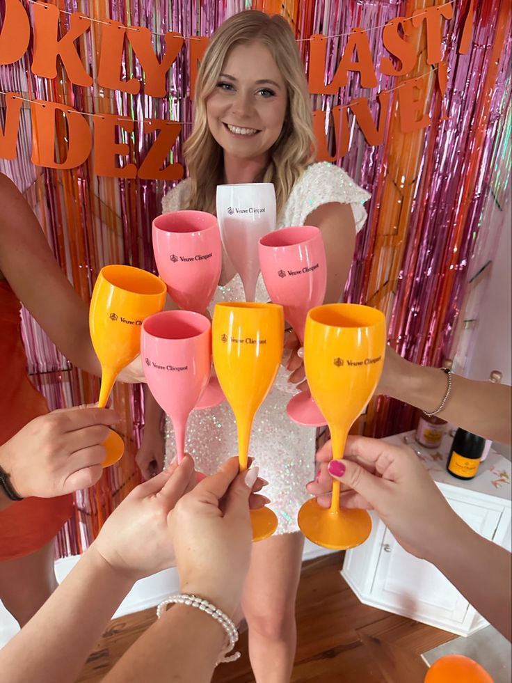 a group of people holding up wine glasses in front of a pink and orange backdrop