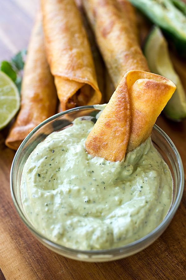 a bowl filled with green sauce next to some pita chips and lime wedges