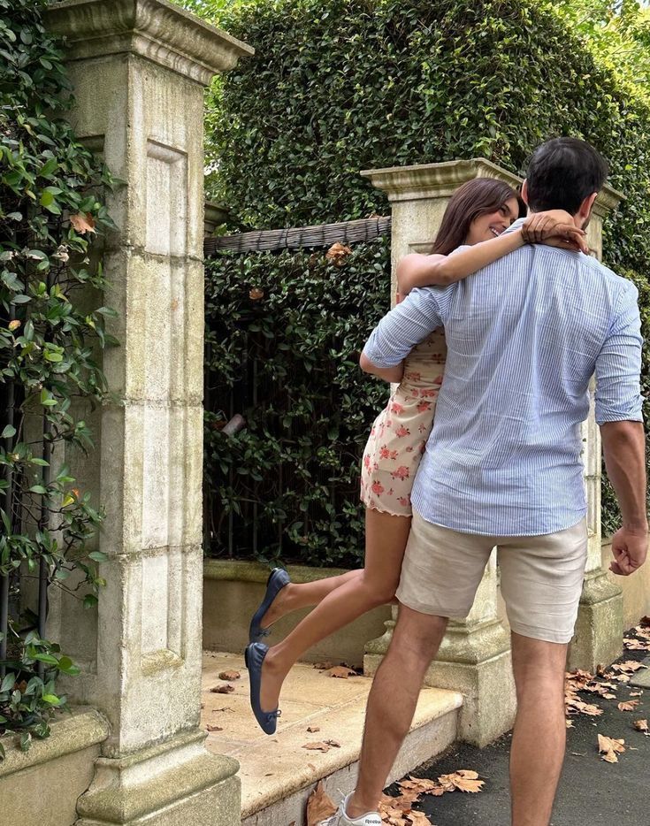 a man and woman standing next to each other on the sidewalk with their arms around each other