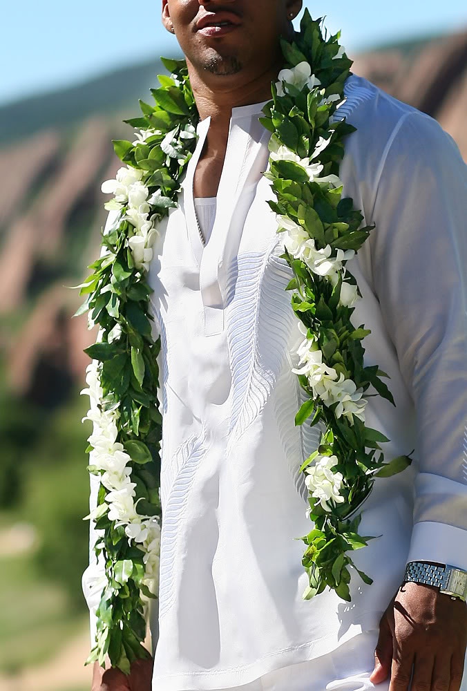 a man wearing a lei and standing in front of the ocean with his hands on his hips