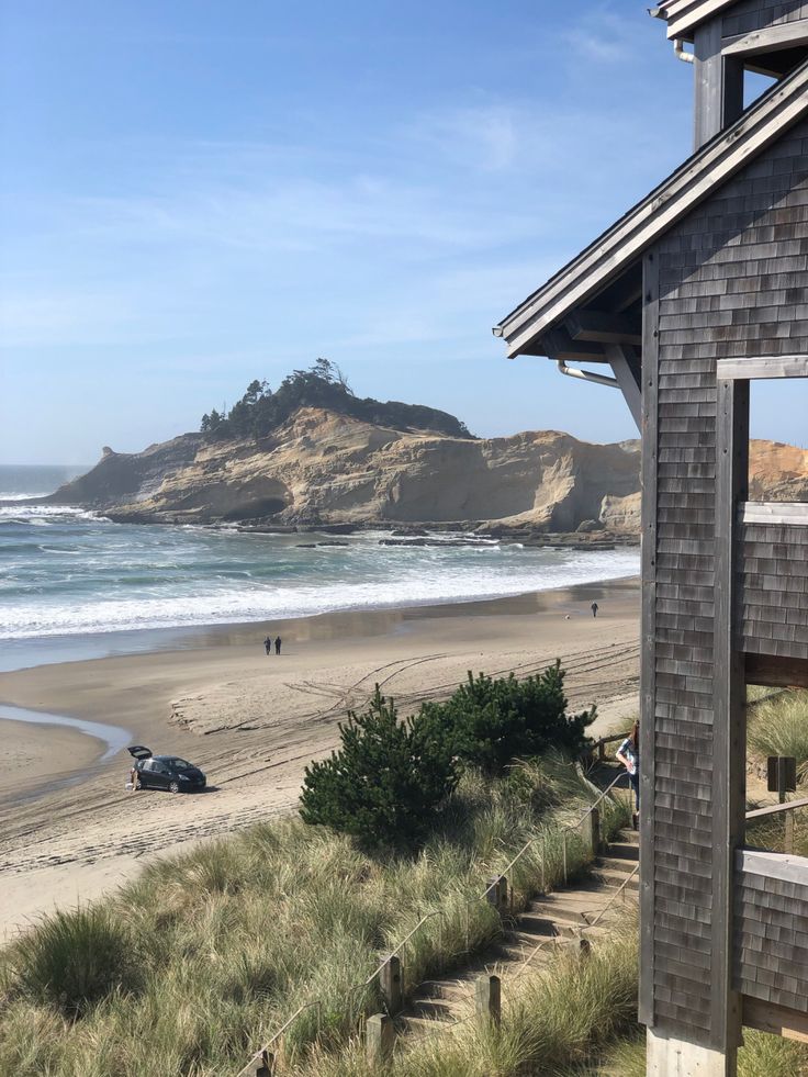 a house on the beach next to an ocean with people in it and one car parked outside