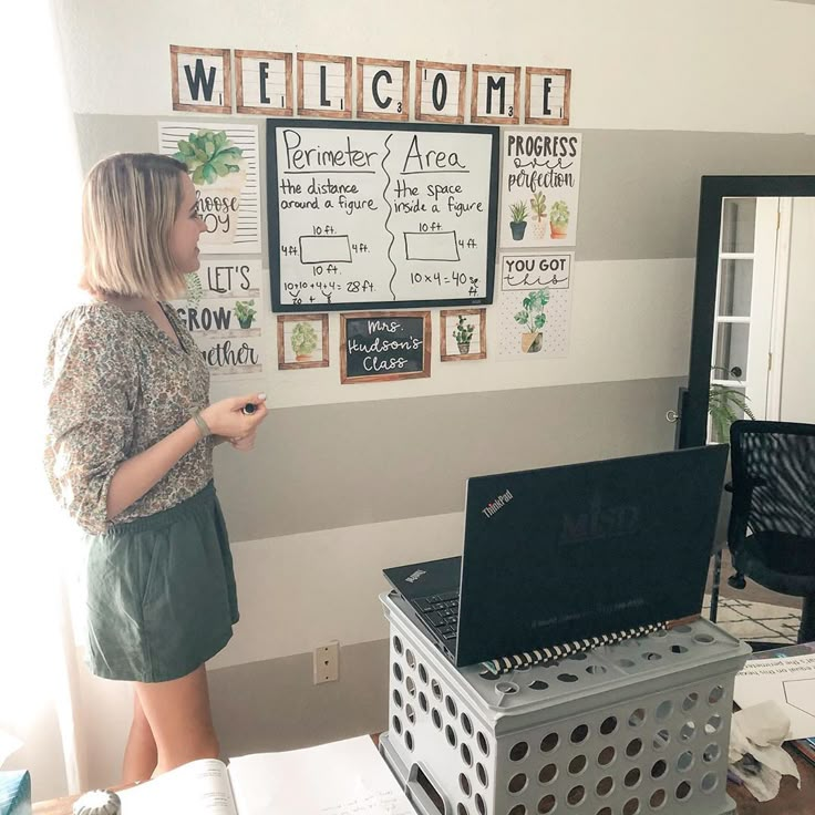 a woman standing in front of a laptop computer on top of a white desk next to a window