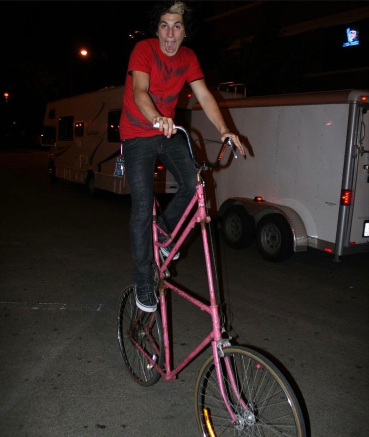 a man on a pink bike in the street at night with an rv behind him