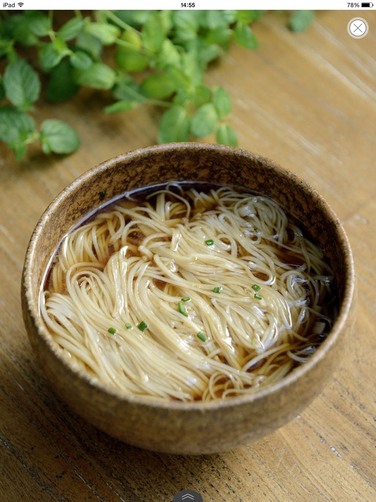 a wooden bowl filled with noodles on top of a table next to some green leaves