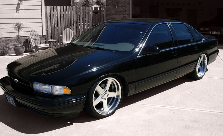 a black car is parked in front of a house with white rims on it