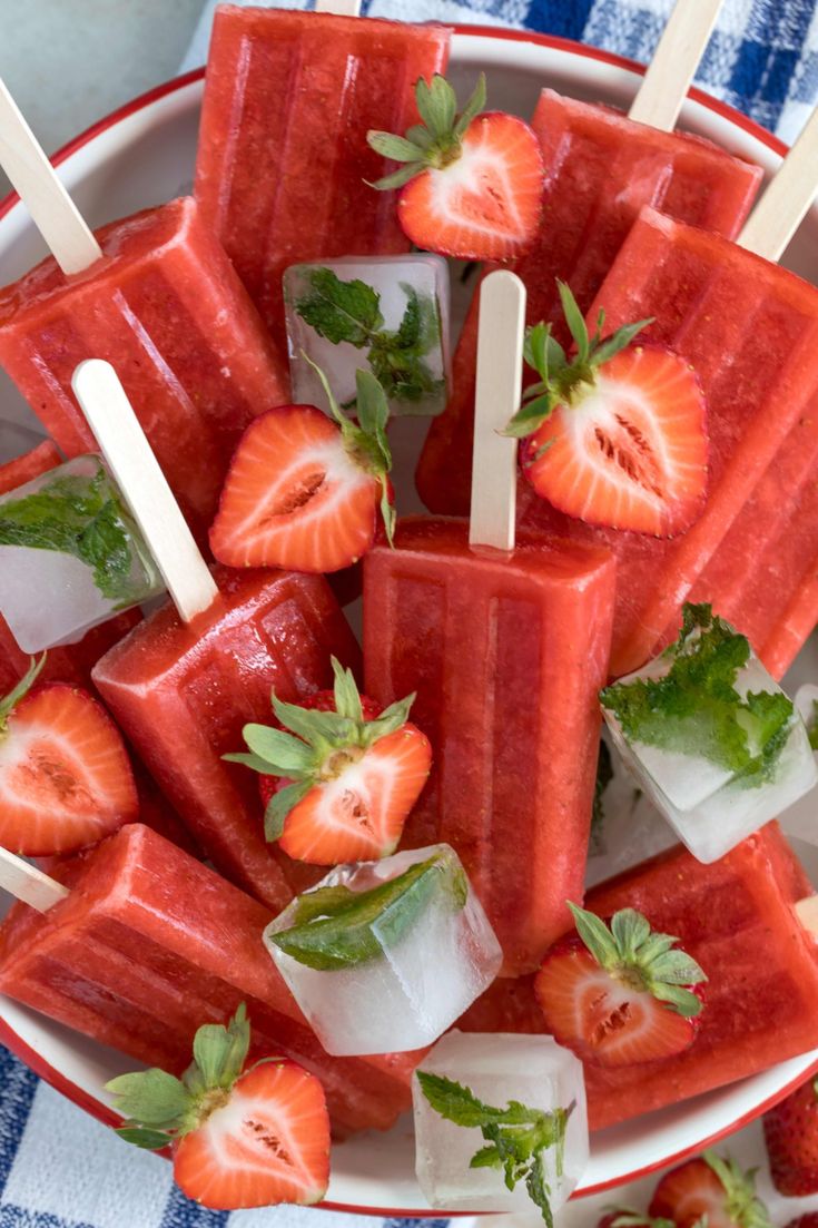 watermelon popsicles with strawberries on top in a white and red bowl