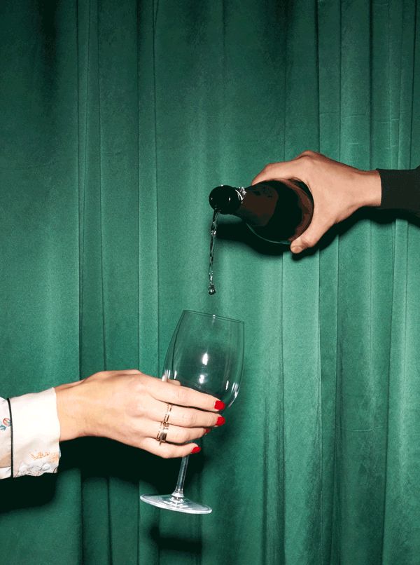 a woman pouring wine into a glass with another person's hand next to it