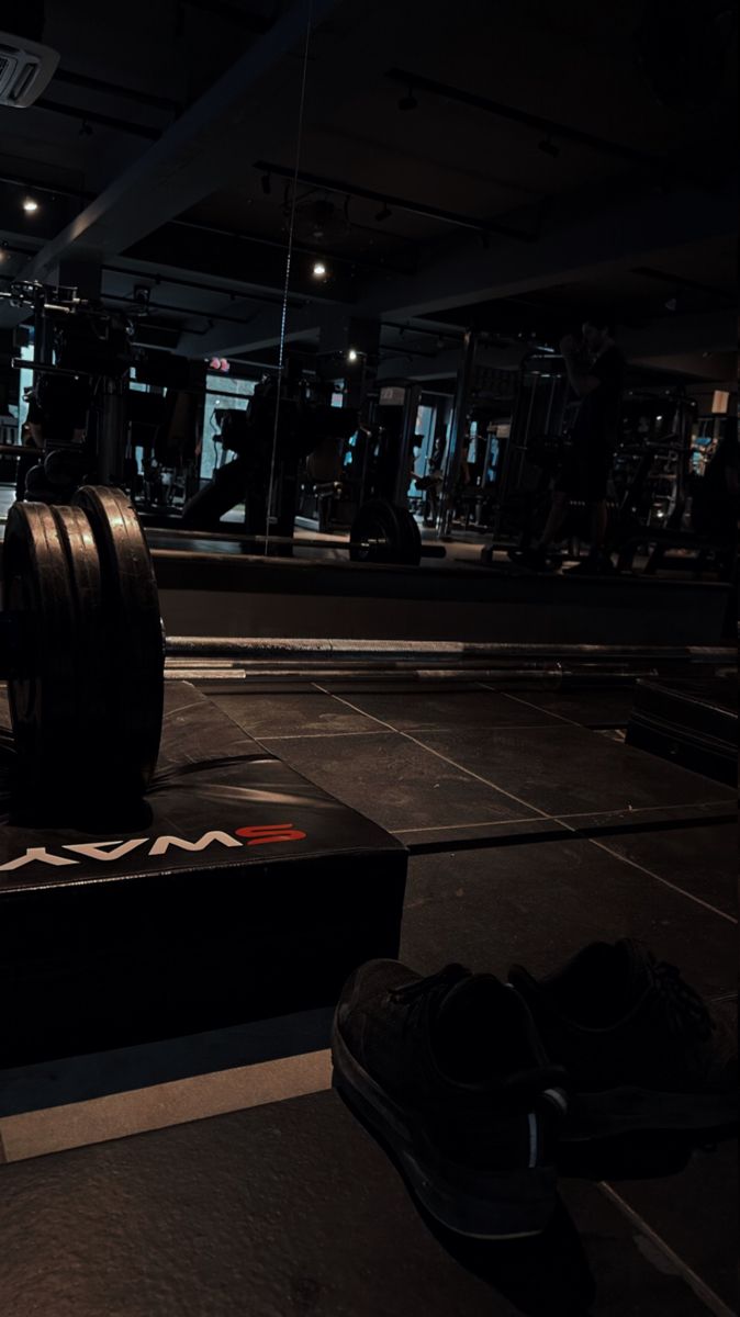 an empty gym with two rows of barbells in the foreground and one row of shoes on the ground