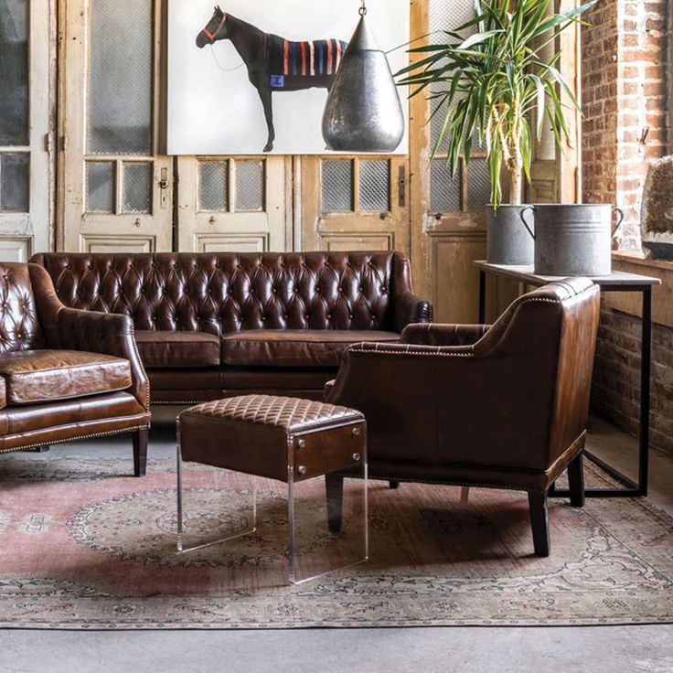 a living room with brown leather furniture and large painting on the wall above it's fireplace