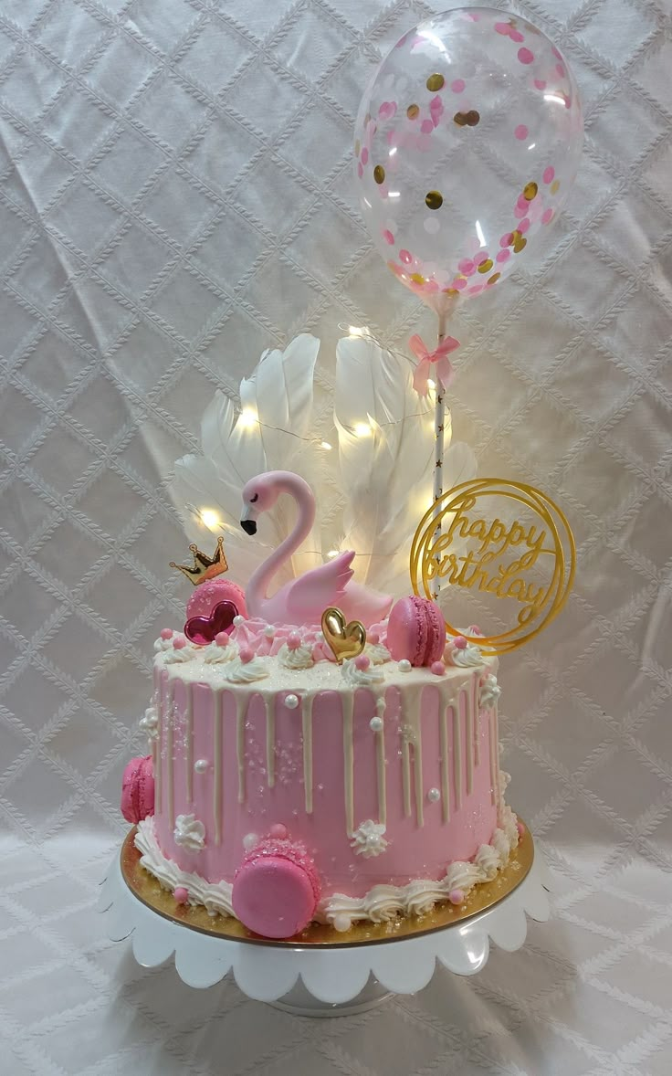 a pink birthday cake with flamingos and balloons