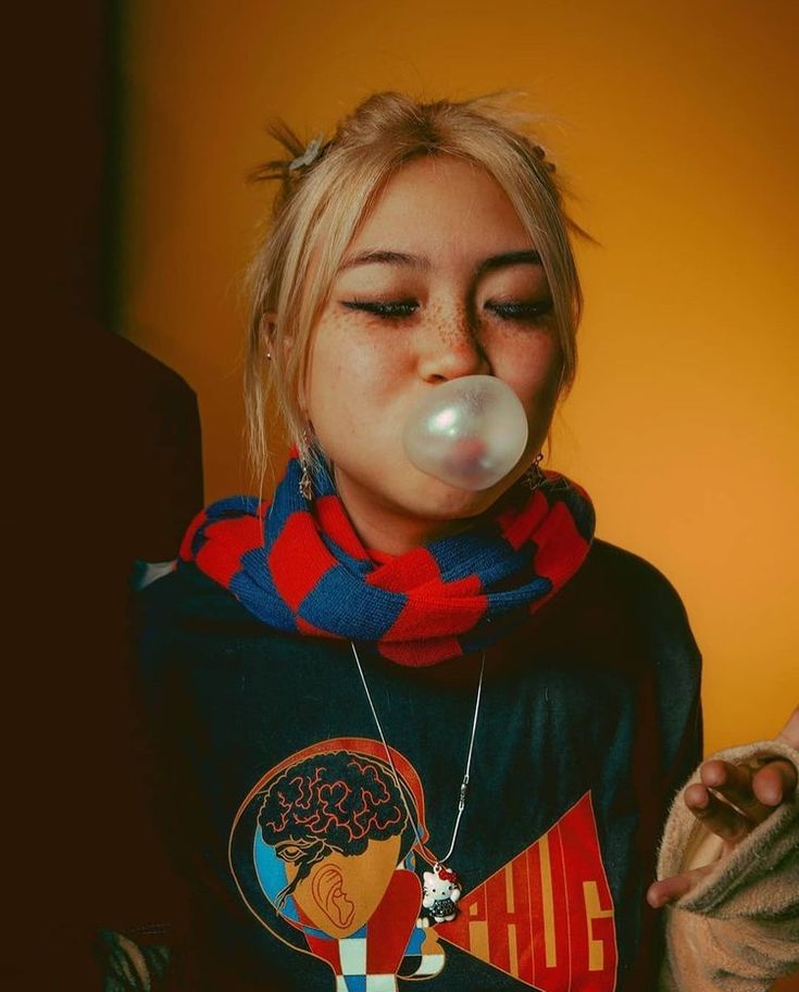 a woman blowing bubbles in her mouth while wearing a black shirt and red, white, and blue scarf