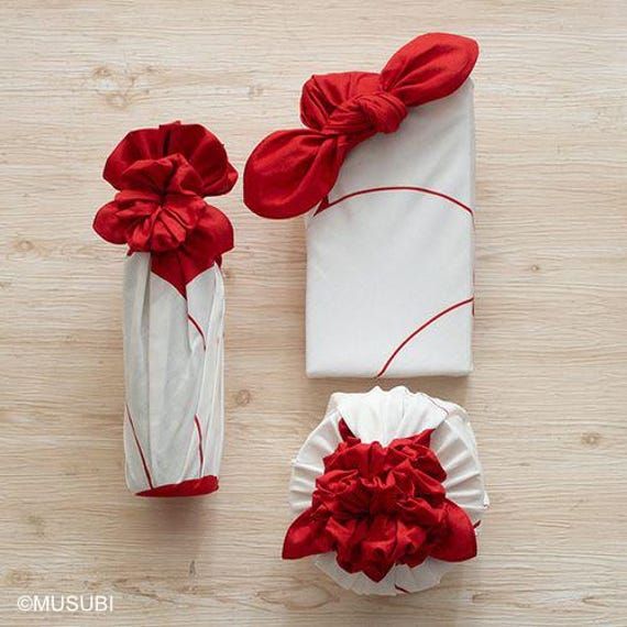 two wrapped presents sitting on top of a wooden table next to white paper and red bows