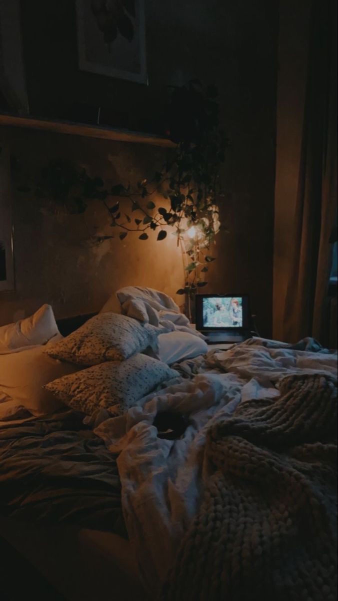 an unmade bed in a dark room with a laptop computer on the end table