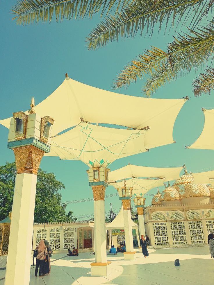 people are standing under white umbrellas in the sun outside an ornate building with palm trees