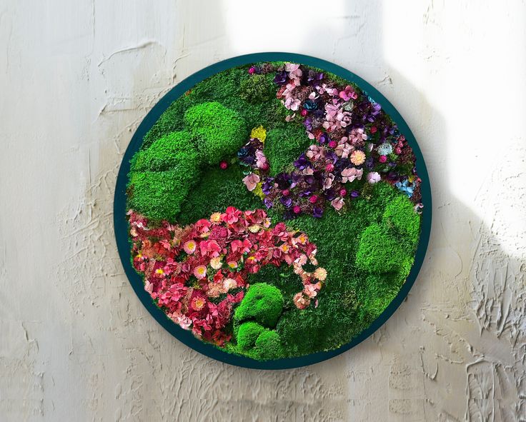 a green plate with flowers and plants on the top is hanging on a wall in front of a window