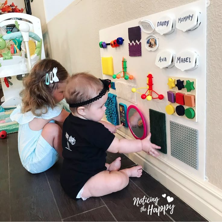 two young children playing with toys on the floor in front of a playroom wall