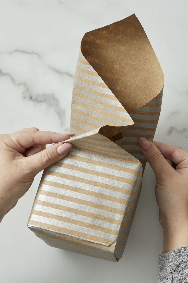 two hands holding wrapped gift boxes with brown and white stripes on them, one is open to reveal the wrapping paper