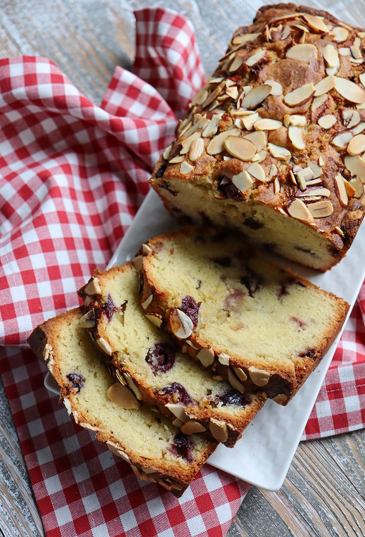 sliced loaf of bread with almonds and cranberry topping on red checkered napkin