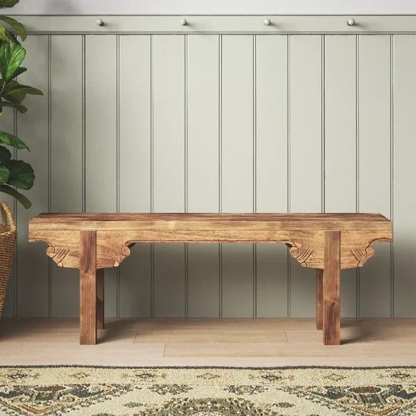 a wooden bench sitting next to a potted plant on top of a rug in front of a wall