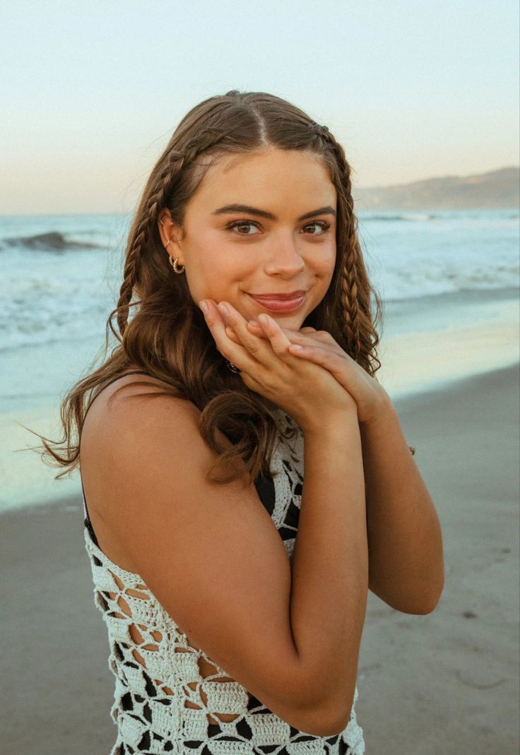 a woman standing on top of a beach next to the ocean with her hands under her chin