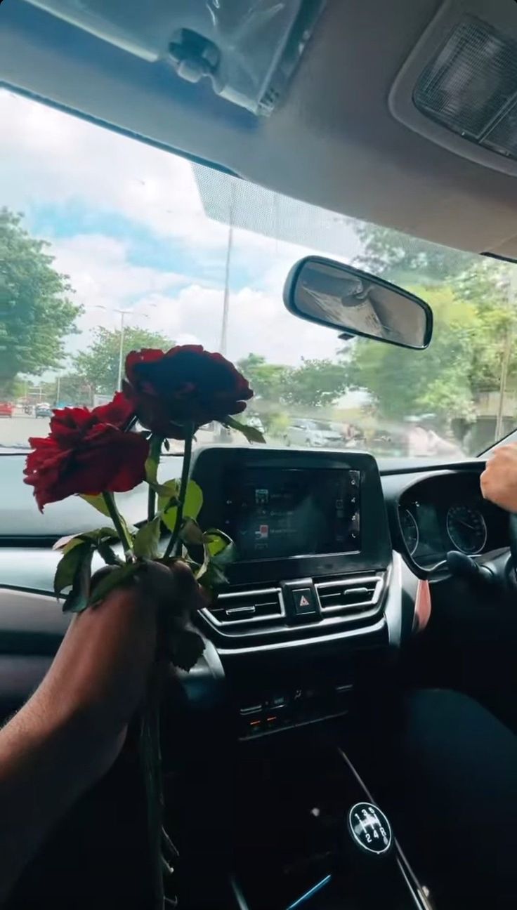 a man driving a car with two roses in the passenger's side view mirror