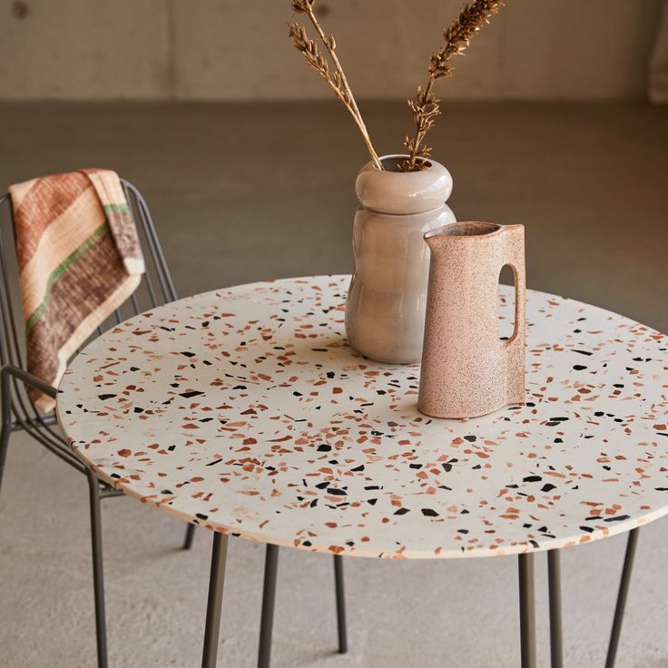 two vases sitting on top of a white table next to a black metal chair