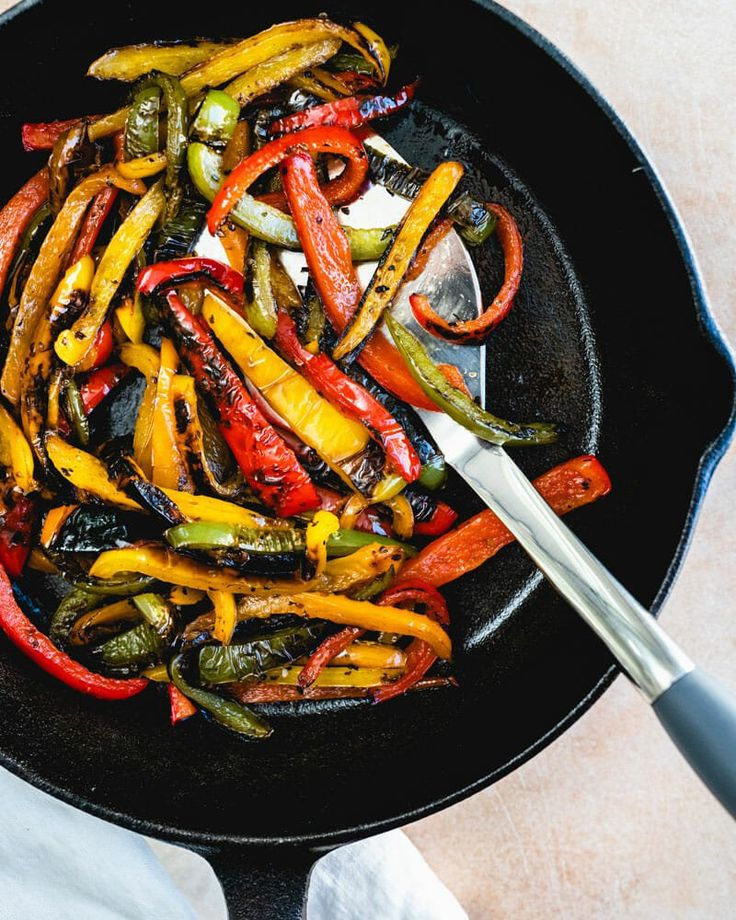 a skillet filled with assorted peppers on top of a table next to a spoon