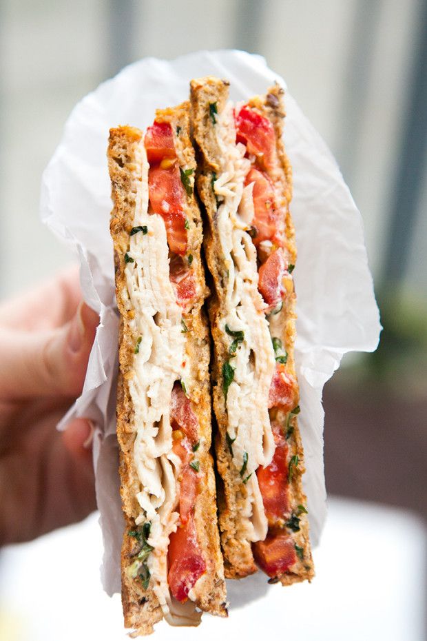 a person holding up a sandwich with cheese and tomatoes