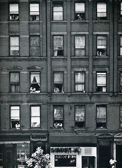 an old black and white photo of people looking out the windows of a tall building