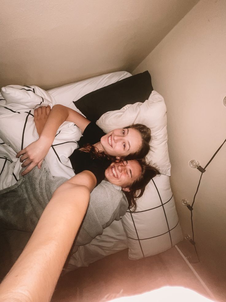 two women laying in bed with their arms around each other and smiling at the camera