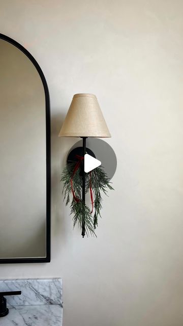 a lamp hanging from the side of a wall next to a mirror with a christmas wreath on it